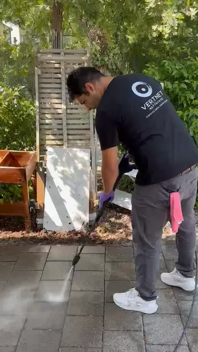 Un employé Vertnet en t-shirt noir manie une lance haute pression dans une cour pavée