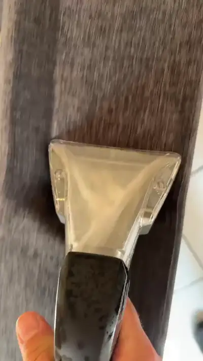 Suceur d’injection-extraction tenu à la main sur un tissu d’ameublement, eau sale visible dans la buse